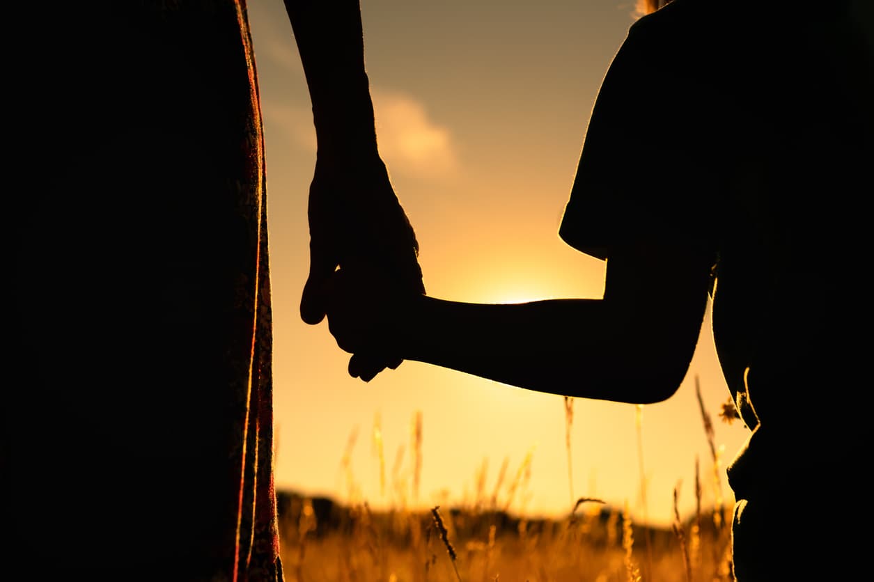 Silhuett av en vuxen och ett barn som håller varandra i handen vid solnedgången, vilket symboliserar adoption och juridisk trygghet. Bilden representerar vikten av Apostille på adoptionsdokument för att säkerställa giltighet i internationella adoptionsprocesser.