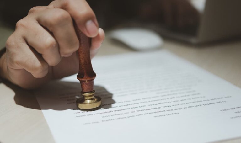 Närbild av en hand som stämplar ett juridiskt dokument med en officiell sigillstämpel, vilket symboliserar apostille-certifiering. I bakgrunden syns en person som arbetar vid en laptop. Perfekt bild för blogginlägget 'Apostille för företag – din guide till smidig internationell affärsverksamhet' på Apostille24.se, som förklarar processen för att legalisera dokument för internationell användning.