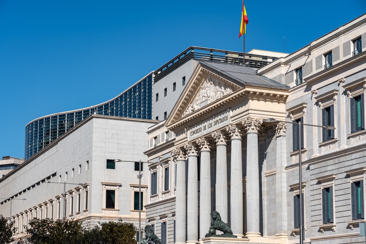 Fasad av Spaniens parlament "Congreso de los Diputados" i Madrid, med spanska flaggan vajande på taket – en symbolisk plats för juridiska och administrativa ärenden som NIE-nummer och legalisering av dokument.